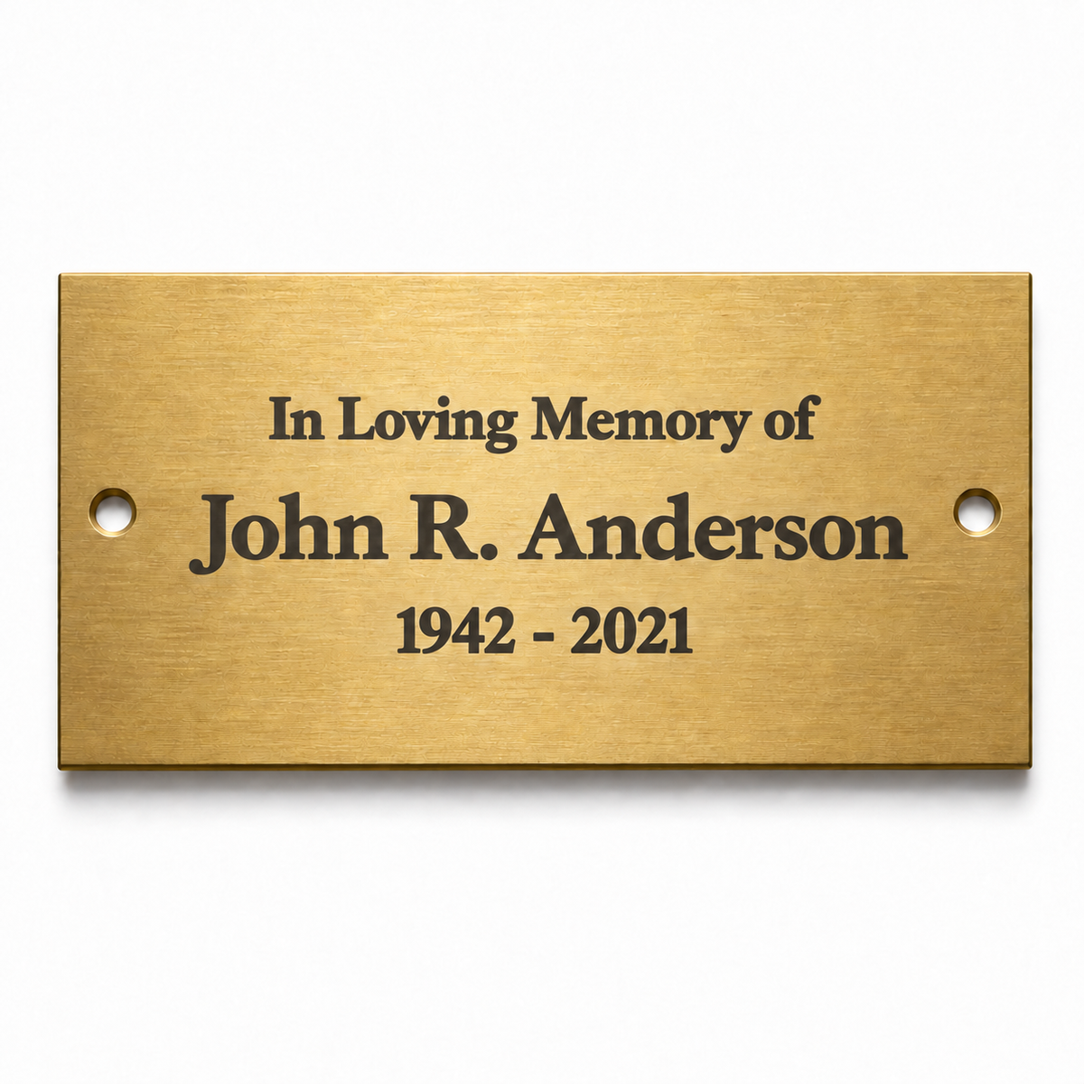 A rectangular brushed gold metal memorial plaque with pre-drilled holes on the sides, featuring the engraved black text 'In Loving Memory of John R. Anderson 1942 - 2021' on a clean white background.
