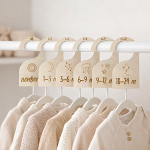 Set of baby clothes on hangers with size labels on a white rack.