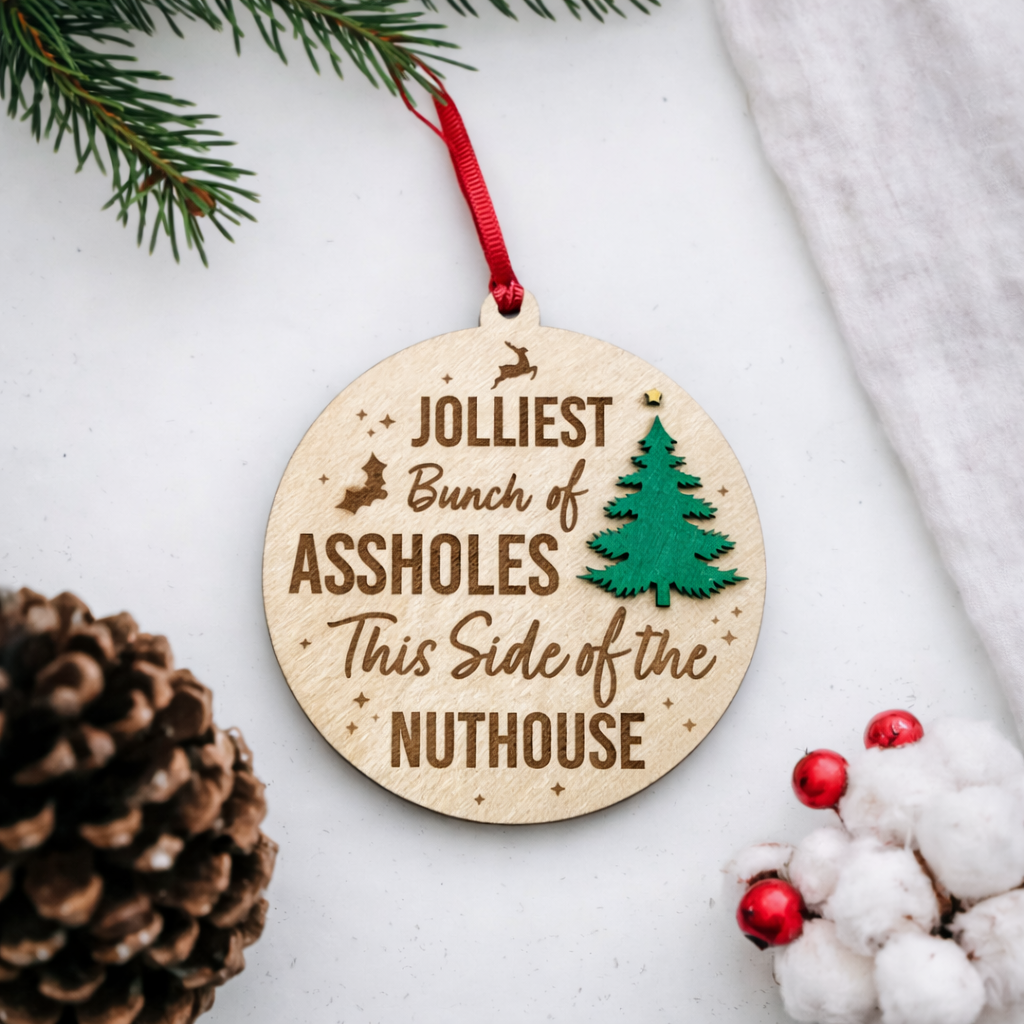 Wooden Christmas ornament with humorous text on a white surface with festive decorations.