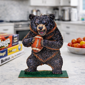 Statue of a bear holding a football on a kitchen counter with board games and tomatoes in the background.