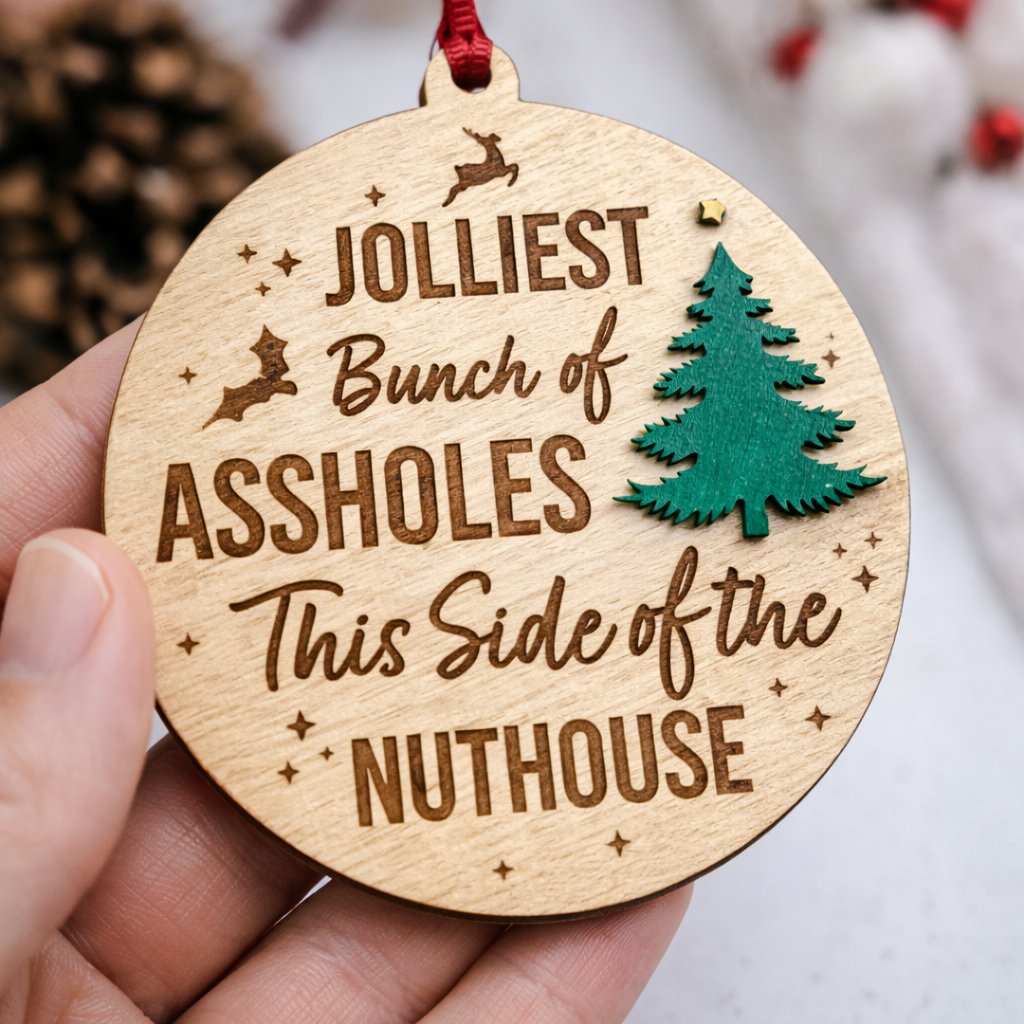 Wooden ornament with humorous text and Christmas tree design, held by a hand.