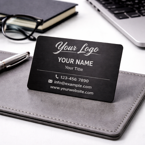 Black business card with customizable text on a desk with a pen, notebook, and glasses.
