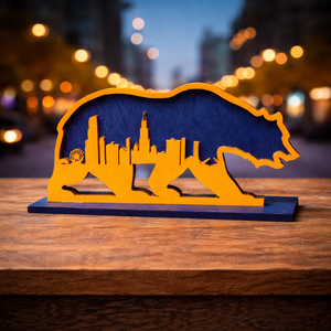 Yellow bear-shaped object with city skyline design on a wooden surface, blurred lights in the background