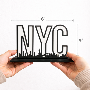 Hands holding a black NYC skyline shelf sign showing true size with measurement lines indicating 6 inches wide by 4 inches tall against a white background.