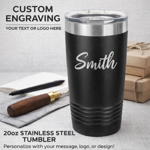 Black stainless steel tumbler with 'Smith' engraved on it, placed on a gray surface with a pen and boxes in the background.